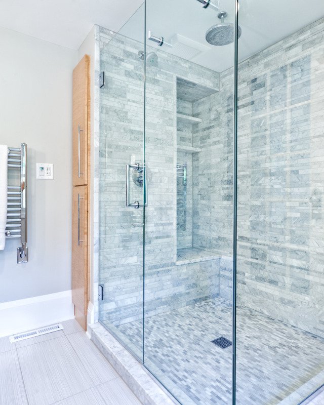 A bath remodel in Falls Church, VA with a large walk-in shower that is glass enclosed with stone tiling.