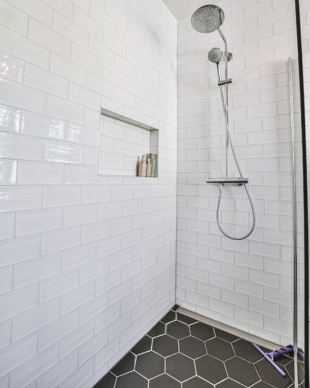 A white subway tile shower with a chrome shower head and a black marble tile floor in Arlington, VA.